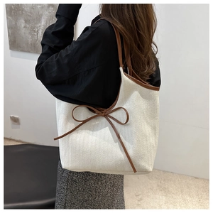 Detail of a large cream tote bag with brown leather bow and herringbone texture shown on model