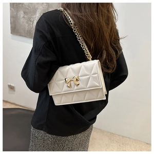 Detail of off-white quilted crossbody bag featuring a gold bow clasp and metal chain strap