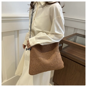 Detail der handgeflochtenen Strohtasche mit gestreiftem Gurt, am Model getragen