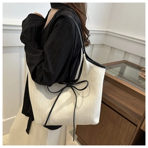 Detail of cream herringbone tote bag with black leather straps and knot ribbon decoration