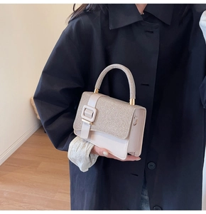 Detail of beige square handbag featuring woven texture flap and large buckle on black coat