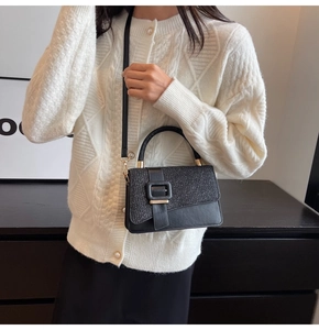 Detail of a black square handbag with glitter texture and gold buckle on a white knit cardigan