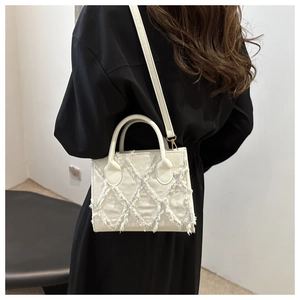 Detail of frayed edge denim crossbody bag in cream white showing tassel texture