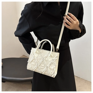 Detail of a beige denim tote bag with frayed diamond patterns and gold hardware straps