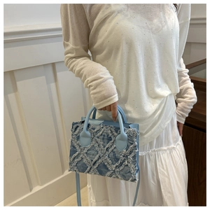 Detail of light blue denim crossbody bag with quilted tassel texture and top handle