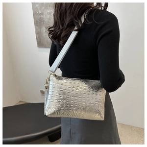Detail of silver crocodile-embossed bag with wide fabric strap and metallic texture