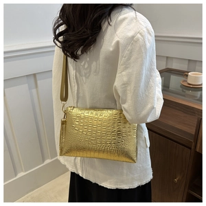 Detail view of the gold crocodile pattern clutch with detachable shoulder strap and zip closure