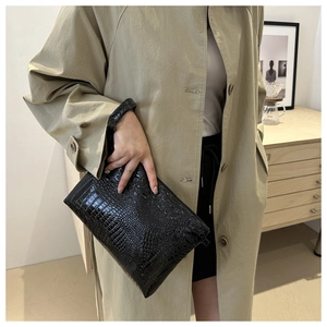 Detail of black crocodile texture envelope bag with wristlet held by a model in a trench coat