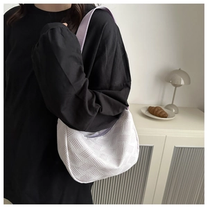 Detail of white tote bag with quilted texture and purple strap worn by a model