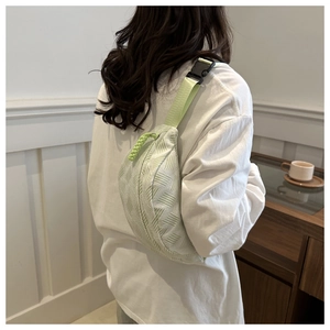 Detail of light green woven fabric crossbody bag with adjustable strap and braided zipper pull