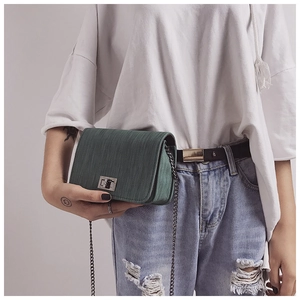 Detail of dark green textured crossbody bag with silver clasp and chain on model