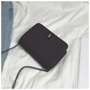 Detail of black chain bag with metallic clasp and textured finish on a fabric background