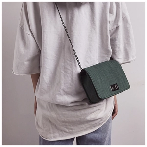 Detail of dark green cross-body bag featuring vertical texture and silver metal twist lock