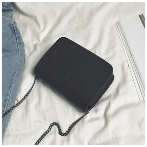 Detail of black rectangular crossbody bag with vertical striped texture and metal chain