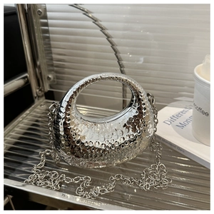 Close-up of silver crescent chain bag with hammered metallic texture on glass stand