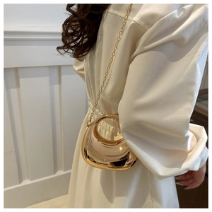 Close-up of elegant gold crescent evening clutch bag with metal chain strap on white dress