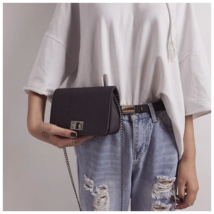 Detail of dark textured crossbody bag with metal chain strap and twist-lock on model