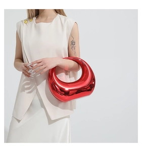 Détail du sac à main rouge métallique avec fini miroir et poignée circulaire porté par mannequin