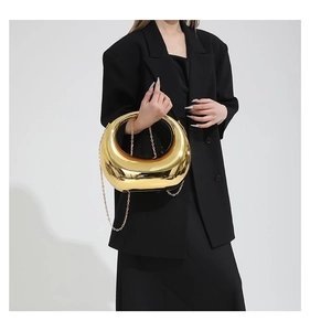 Détail d'un sac à main demi-lune doré brillant avec bandoulière chaîne sur un blazer noir