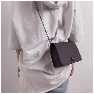 Detail of a black crossbody bag with textured finish, rotating lock, and metal chain