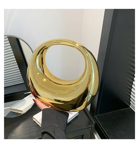 Détail d'un sac à main rond doré miroir moderne tenu dans un cadre intérieur élégant