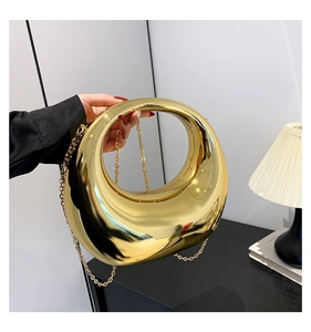 Gros plan d'un sac à main rigide en croissant doré poli miroir avec bandoulière chaîne