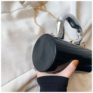 Detail shot of black acrylic box bag with silver arched handle and gold chain strap