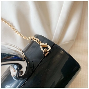 Close-up of golden metal chain and lobster clasp on black glossy acrylic clutch bag