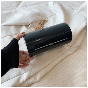 Detail of a black cylinder acrylic clutch bag with a slim gold chain strap in hand