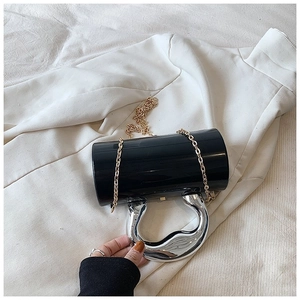 Detail of black acrylic cylindrical clutch featuring a unique silver metallic wavy handle