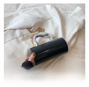 Close-up of black acrylic cylinder bag with silver metal handle and gold chain strap