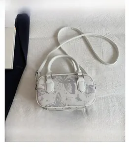Mini white Boston bag with butterfly print shown next to a smartphone for size scale