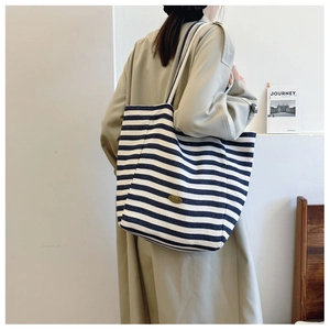 Detail of large blue and white striped canvas tote bag worn by a model in casual style