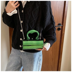 Detail of green metallic cylinder bag featuring a bold organic handle and gold chain strap