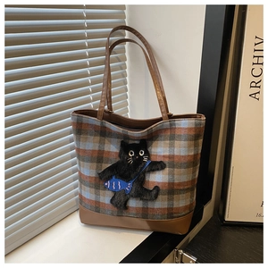 Detail of plaid tote bag featuring a cute black cat patch and premium brown leather trim