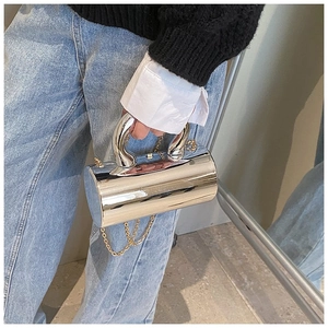 Detail of silver cylindrical acrylic handbag with curved handles and gold chain strap