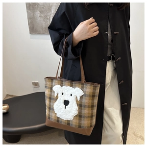 Detail of plaid tote bag with schnauzer patch worn with a long black coat