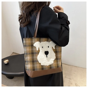 Detail of plaid tote bag featuring fuzzy puppy patch and brown faux leather base