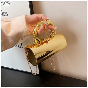 Close-up of a gold mirrored cylindrical evening bag with a thick curved handle and chain