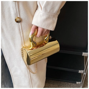 Modern gold cylindrical metal clutch bag with curved handle shown on a model