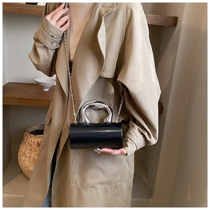 Detail of black acrylic cylinder bag featuring a bold silver metal handle and chain strap