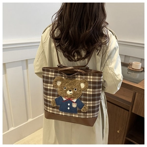 Detail of plaid tote bag with teddy bear patch worn with a beige trench coat