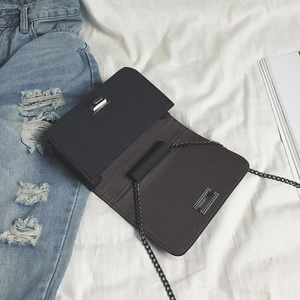 Black rectangular crossbody bag with linear texture and metal chain strap on jeans