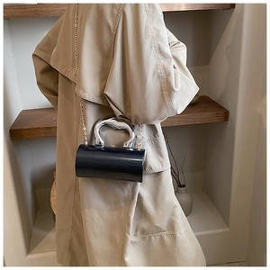 Detail of black cylindrical box bag with silver metallic handle and gold chain strap