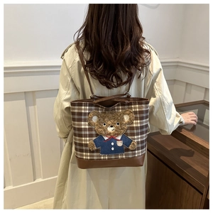 Detail showing plush bear patch on brown checkered tote bag with leather trim