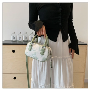 Detail of a white cylinder handbag with green floral print and leather handles