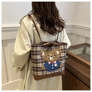 Close-up of brown plaid tote bag featuring a cute 3D plush bear patch in blue uniform