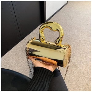 Detail of a shiny gold cylindrical evening bag with a unique wavy metal handle