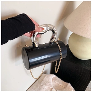 Detail view of a black acrylic cylindrical clutch with chunky silver handle and gold chain