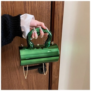 Close-up of green metallic cylindrical clutch with gold chain and rigid handle